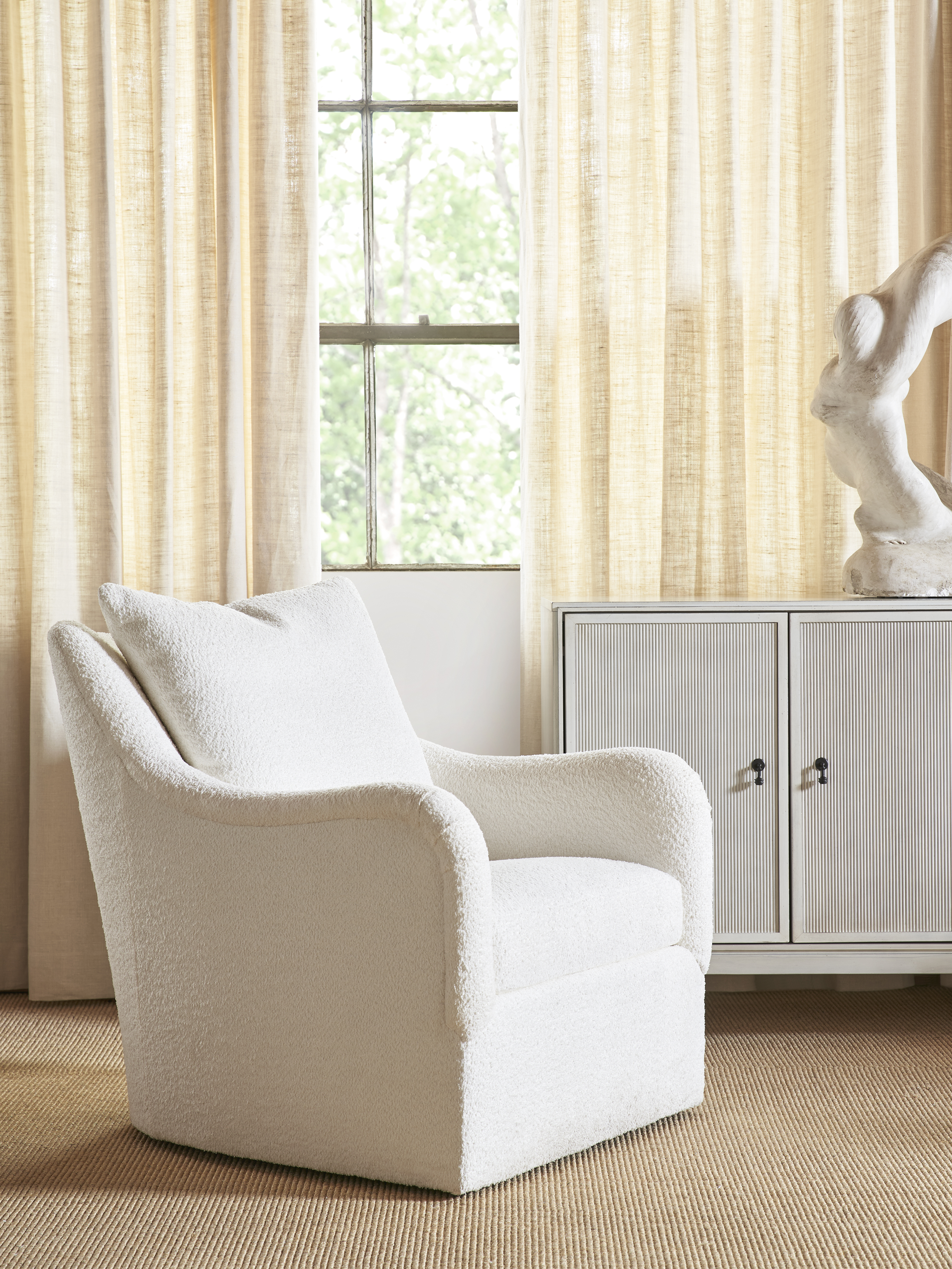 Refined showroom vignette with a white bouclé swivel chair beside a fluted cabinet and sheer linen drapery