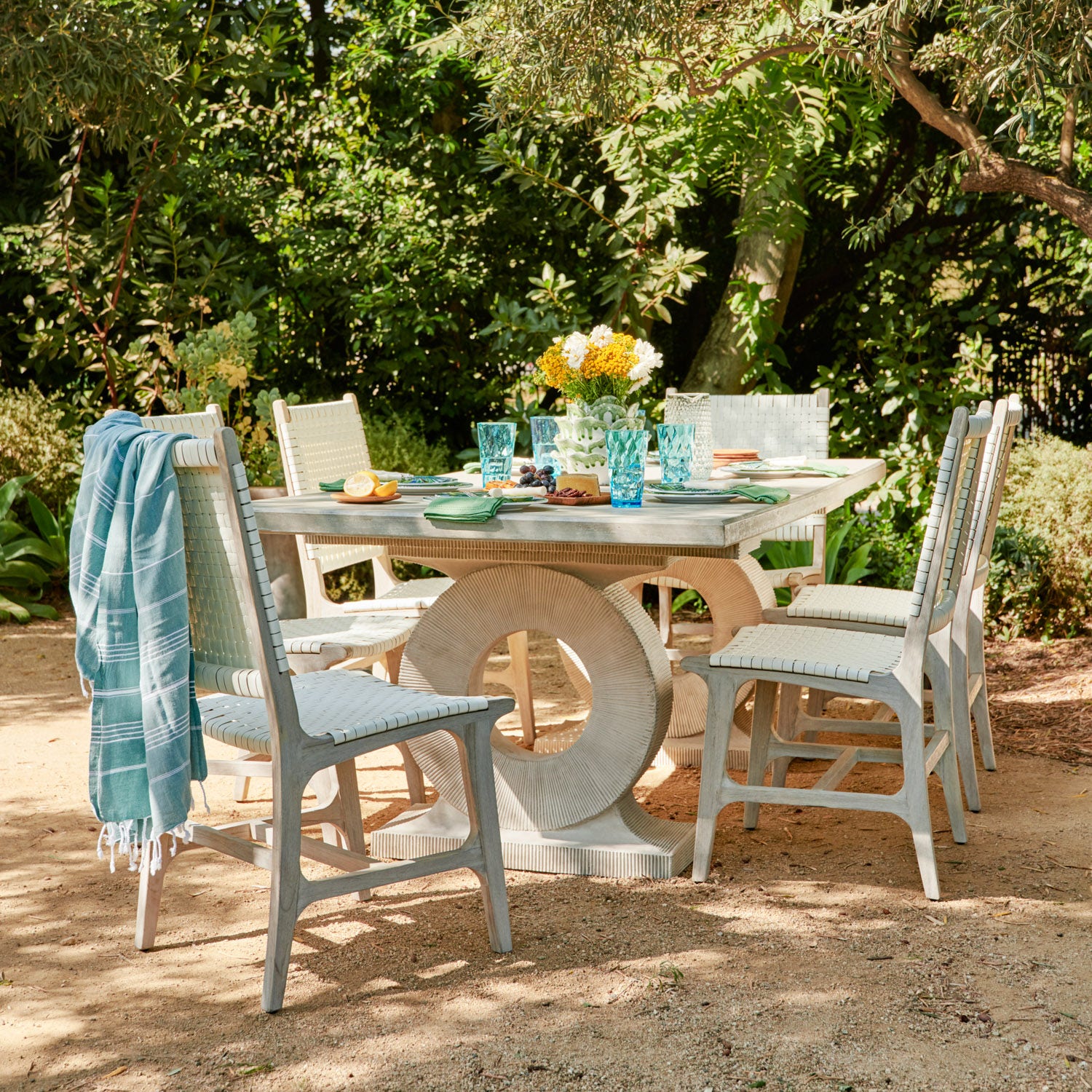 Outdoor dining table and chairs set in a leafy garden with a layered throw and fresh place settings