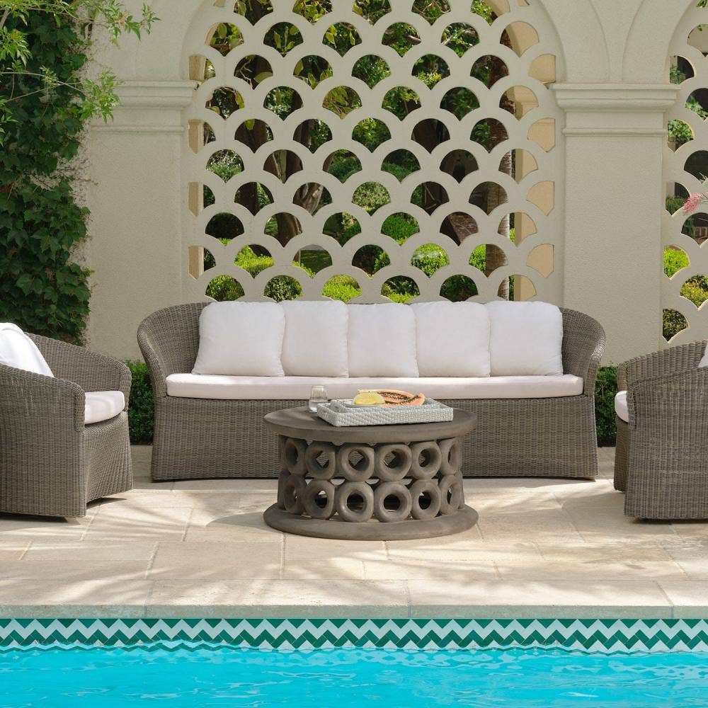 Woven outdoor sofa and lounge chairs arranged as a poolside room against a carved lattice screen and lush garden