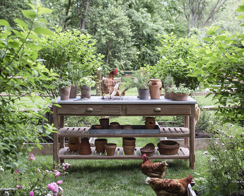 Garden potting table with terracotta pots and herbs surrounded by lush greenery